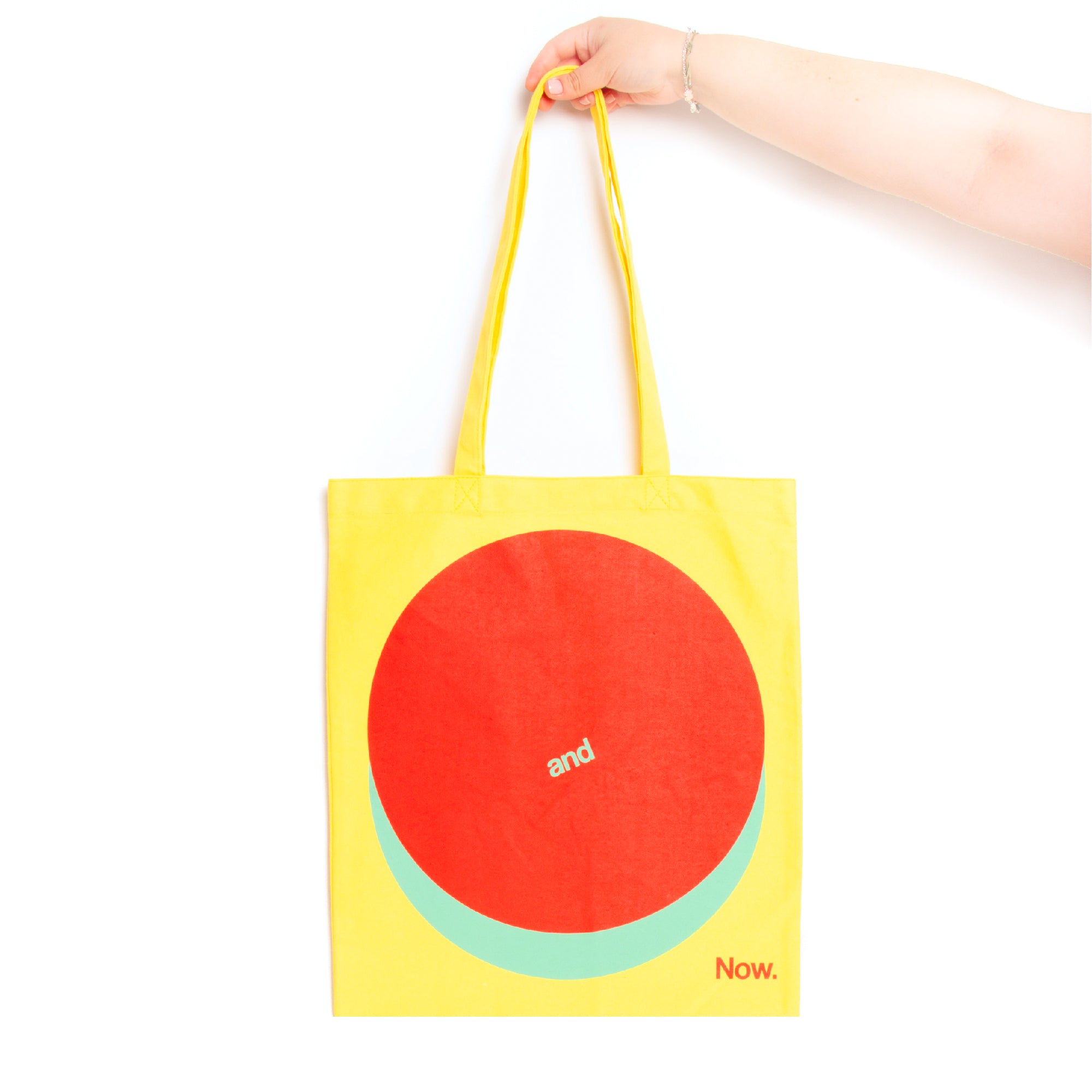 A yellow tote bag with a red and blue geometric design, held by a hand.