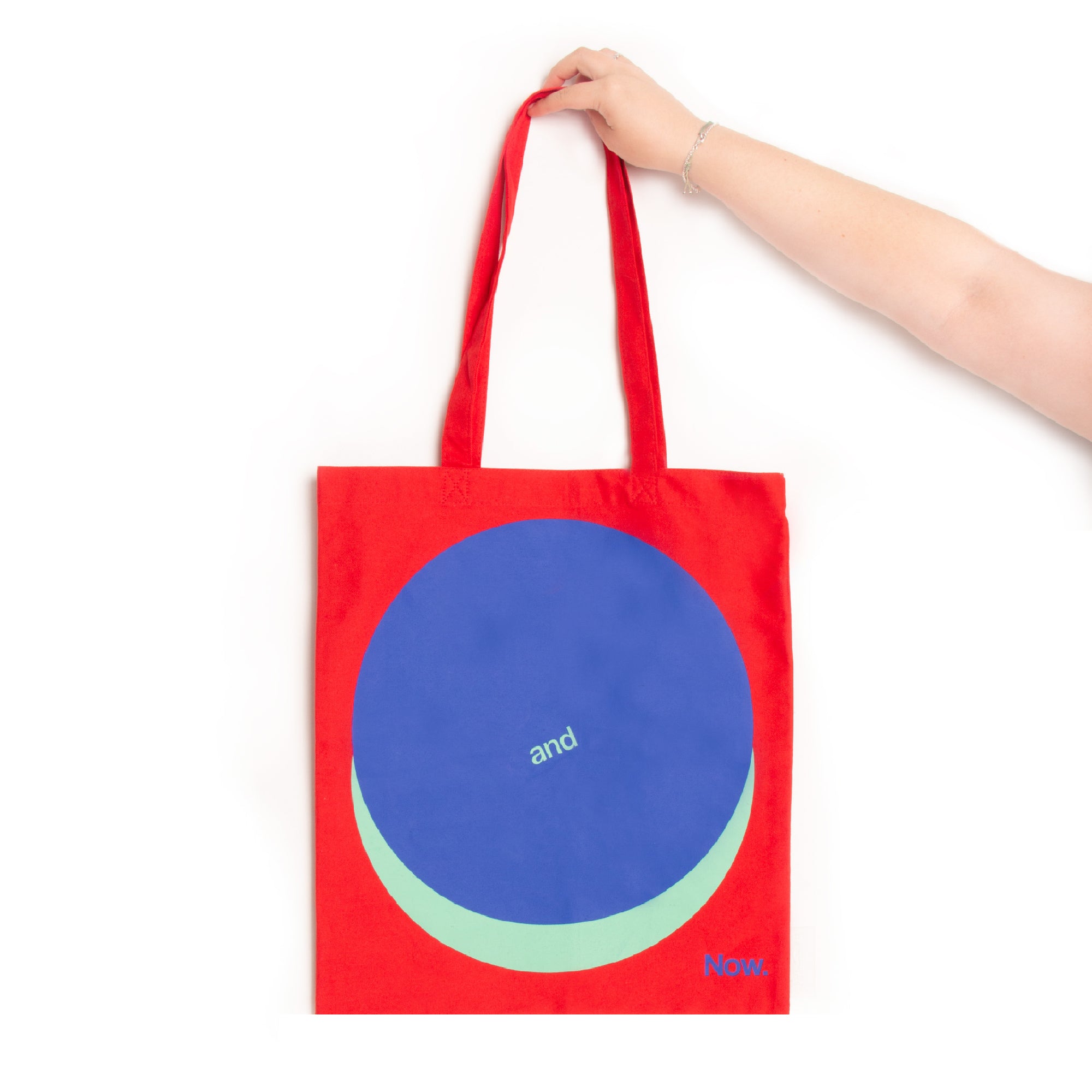 A person holding a red tote bag with a large blue circle and text design on the front.