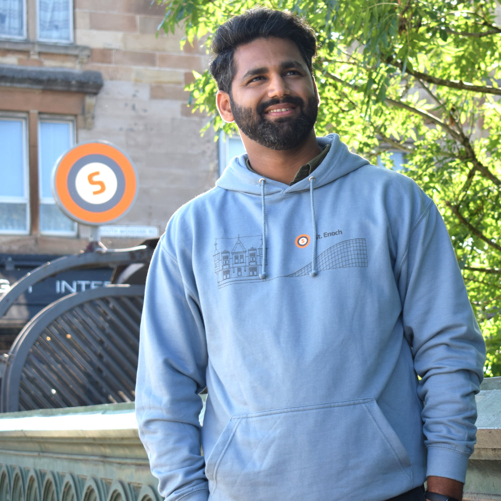 Man wearing blue hoodie standing in front of Glasgow Subway station with subway sign visible in background.