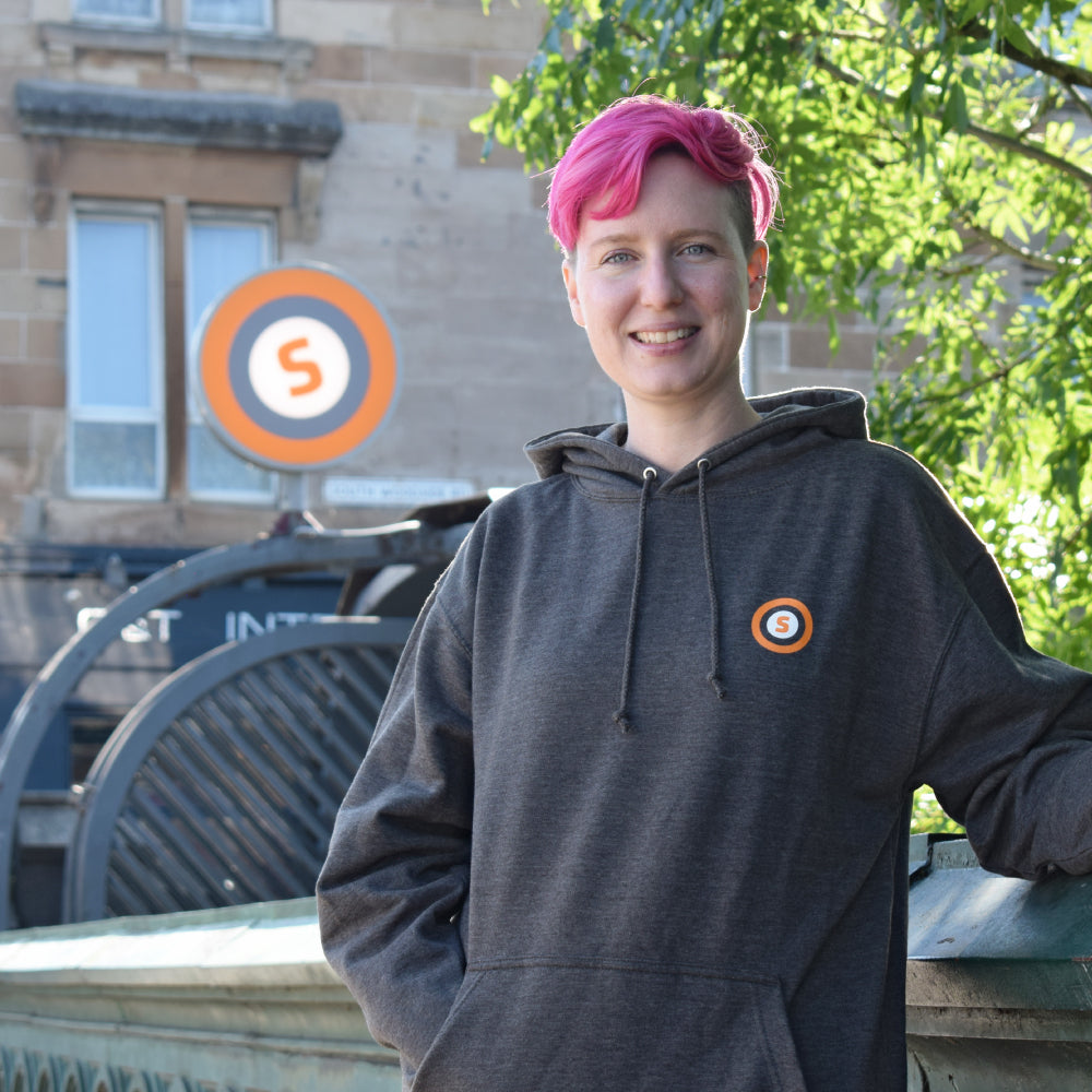 Women in grey hoodie standing in front of Glasgow subway station.