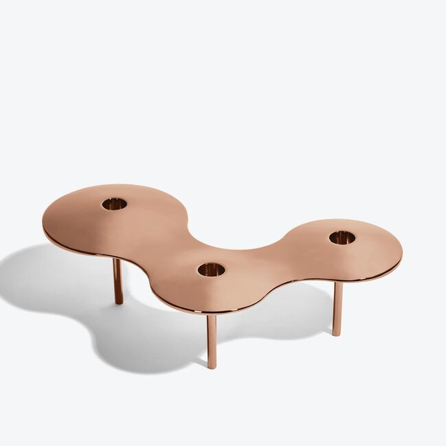 A polished, silver-colored candle holder designed by Zaha Hadid, featuring a smooth, curved structure with two holes to hold candles.