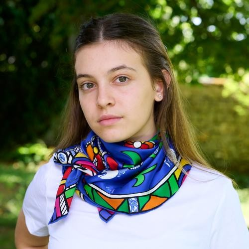 A person wearing a blue silk scarf with a vibrant geometric pattern around their neck.