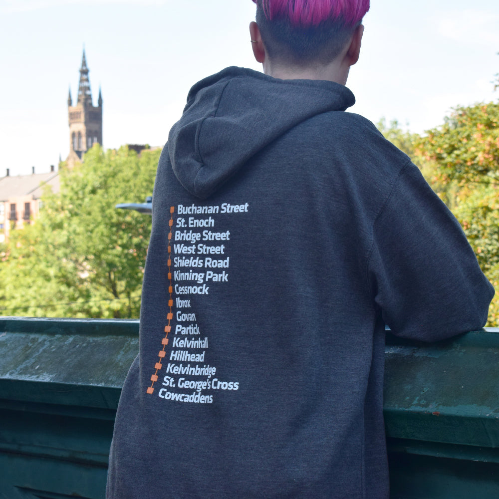 Woman wearing grey hoodie standing outdoors with a steeple visible in the background, modeling Glasgow Subway hoodie.