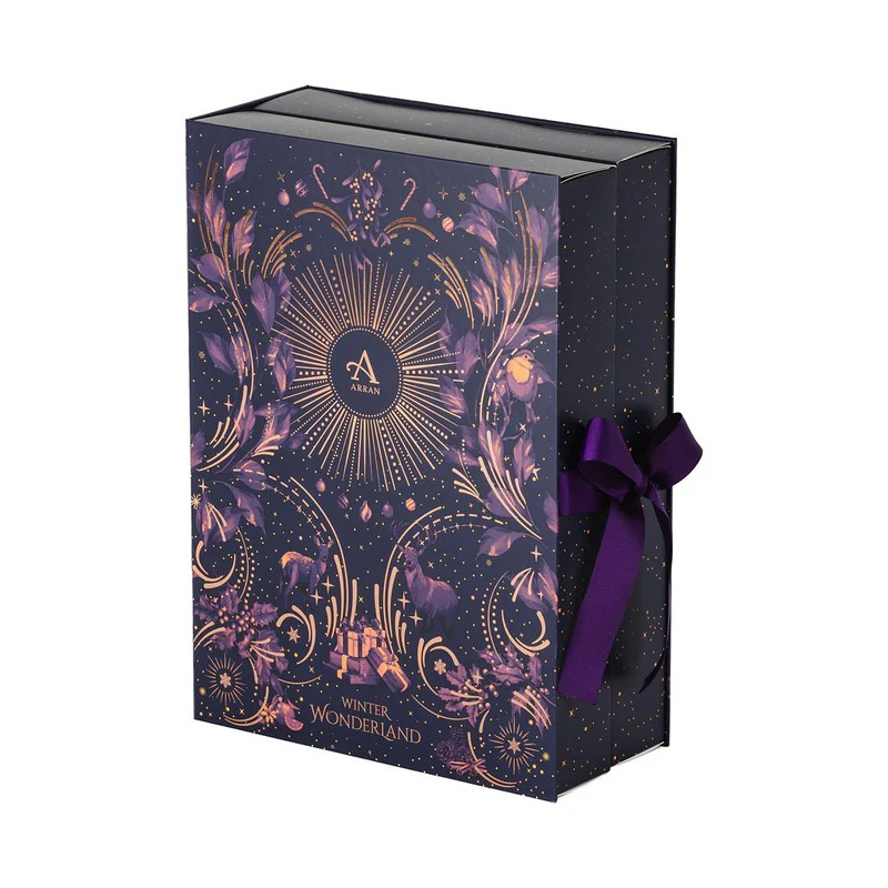 An ornate purple and gold box with floral and geometric patterns, adorned with a purple bow and containing an Arran branded perfume and fragrance advent calendar.