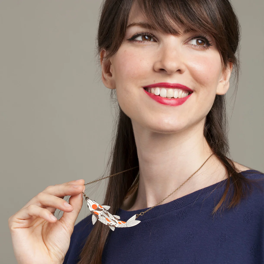 Woman wearing a necklace with a fish pendant against a neutral background