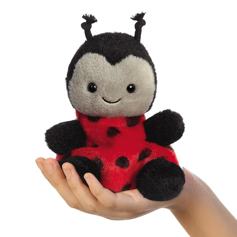 Plush ladybug toy held in a hand on a white background