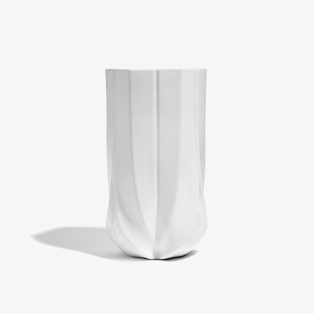 A white, porcelain vase with a gloss finish, featuring a complex geometric design with a distinct base that weaves in an upward motion.