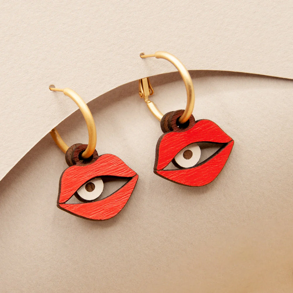 Earrings shaped like red lips with gold accents on a beige background